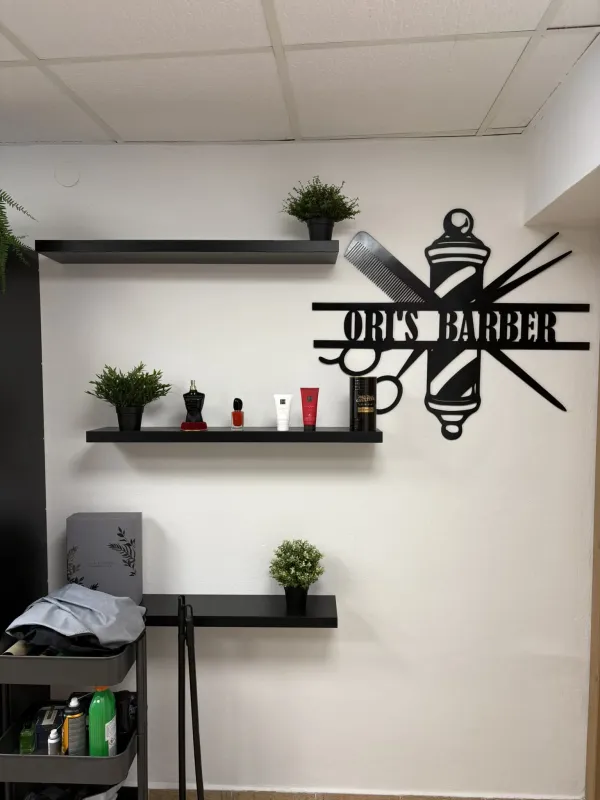 Stylové černé logo Ori's Barber Shop na stěně v interiéru salonu.