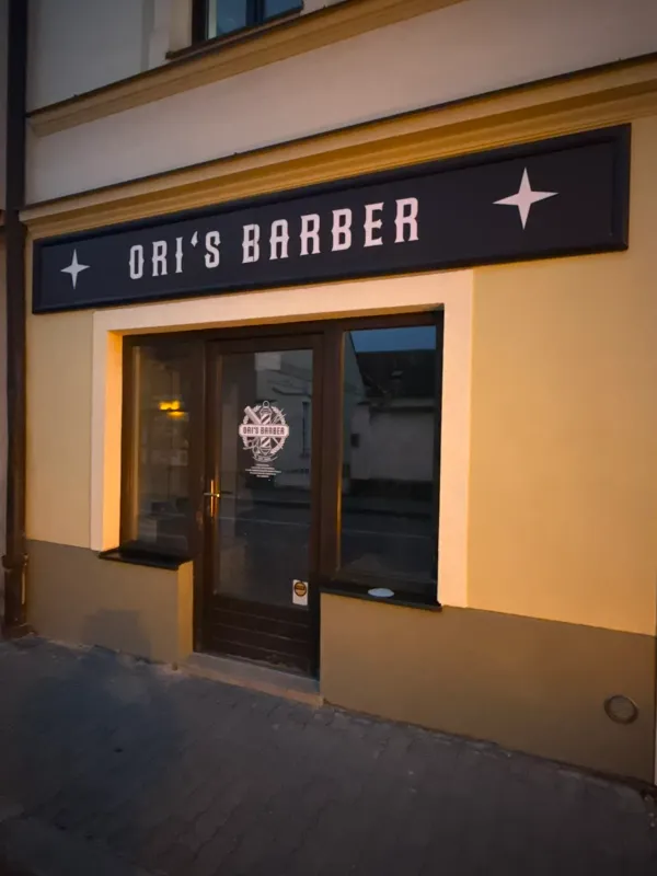 Nasvícený exteriér Ori's Barber Shop v Dobřanech za večerního šera.