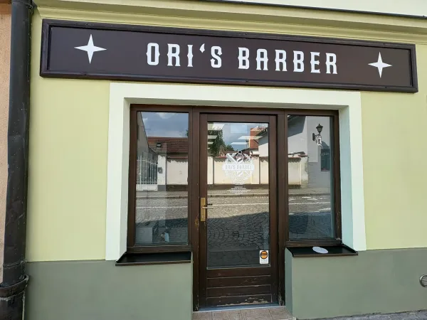 Vchod do Ori's Barber Shop v Dobřanech s charakteristickým vývěsním štítem.